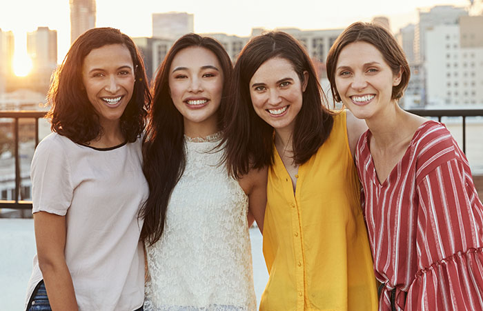 Portrait Of Female Friends Gathered On Rooftop Terrace For Party With City Skyline In Background